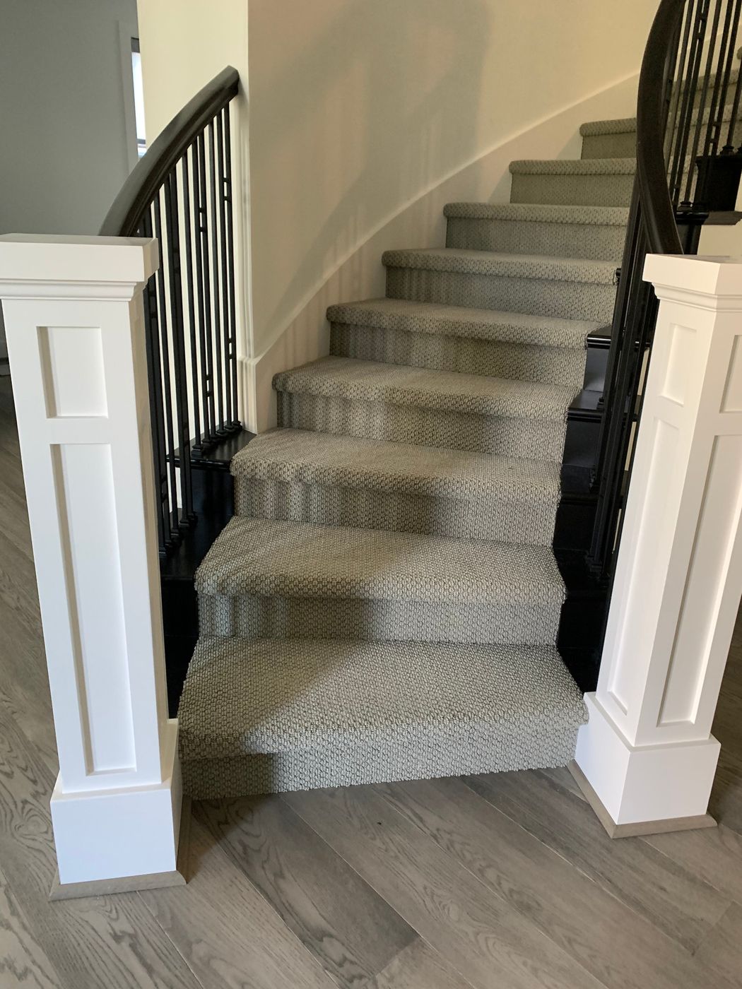 Curved staircase with a carpet runner, white box newels and black balusters